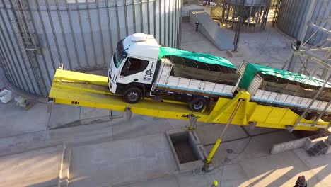 Aerial-shot-of-a-white-truck-unloading-at-an-industrial-silo-during-the-day,-clear-skies