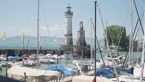 Día-Soleado-En-El-Puerto-De-Lindau-Con-Barcos-Atracados-Y-El-Emblemático-Faro-Y-La-Estatua-Del-León,-Cielo-Azul-Claro