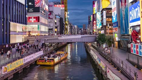 Night-Time-Lapse-Of-Boats-passing,-people-and-Illuminated-signboards-at-Ebisu-Bridge-Dotonbori-Canal-Namba-Osaka,-Japan-TILT