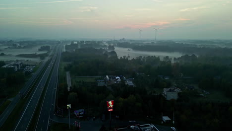 Eine-Luftdrohne-Schoss-Von-Oben-Nach-Unten-über-Autos,-Die-über-Eine-Schnellstraße-Fuhren-Und-An-Einem-Nebligen-Morgen-Durch-Eine-Landschaft-Mit-Im-Hintergrund-Sichtbaren-Windmühlen-Fuhren