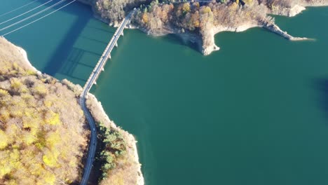 Toma-Aérea-De-Una-Carretera-Y-Un-Puente-Que-Cruza-Un-Río-En-Medio-De-Las-Montañas-Y-Los-Alpes-Mientras-Un-Automóvil-Cruza-El-Puente