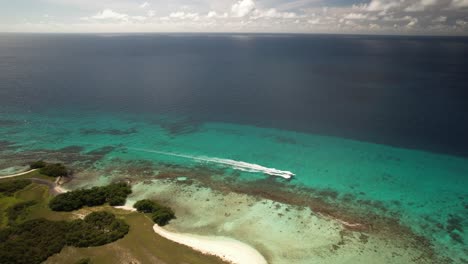 Un-Barco-Navegando-Por-Las-Cristalinas-Aguas-Turquesas-Cerca-De-Las-Exuberantes-Islas-Verdes-De-Los-Roques,-Venezuela,-Vista-Aérea