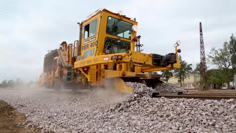 Máquina-De-Colocación-De-Vías-De-Ferrocarril-Amarilla-En-Funcionamiento-En-Un-Día-Nublado,-Esparciendo-Grava-En-Las-Vías