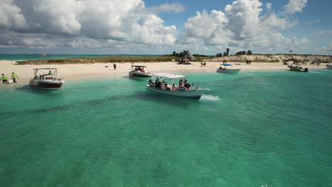 Barcos-En-Aguas-Cristalinas-De-Color-Turquesa-Cerca-De-La-Playa-De-Arena-De-Los-Roques,-Venezuela,-Con-Gente-Y-Cabañas-De-Playa,-Vista-Aérea