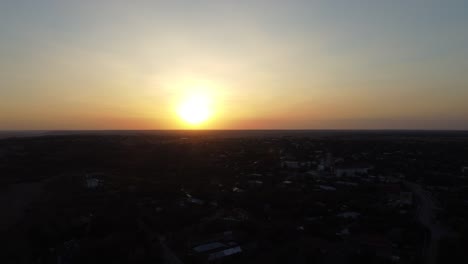 Toma-Aérea-De-Una-Hermosa-Puesta-De-Sol-Sobre-Una-Ciudad-Que-Está-Cayendo-En-La-Sombra