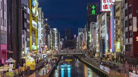 Night-Time-Lapse-Of-Boats-passing,-people-and-Illuminated-signboards-view-from-Ebisu-Bridge-Dotonbori-Canal-Namba-Osaka,-Japan-TILT