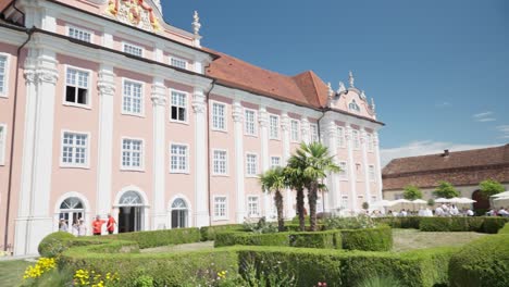 Sunny-day-at-the-pink-Meersburg-Castle-by-Lake-Constance-with-tourists-and-palm-trees-in-the-foreground