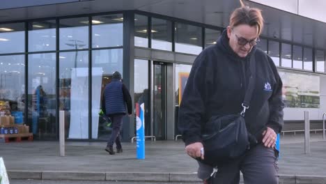 Time-lapse-shoppers-enter-busy-Aldi-supermarket-entrance-with-people-and-cars-passing-outside,-Close-shot