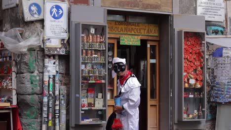 Man-dressed-in-white-costume-and-masquerade-mask-outside-curios-shop