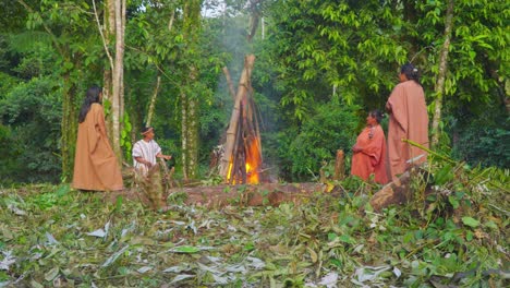 Familia-Tribal-Alrededor-De-Un-Fuego-En-Una-Exuberante-Selva-Peruana,-Con-Un-Niño-En-Traje-Tradicional