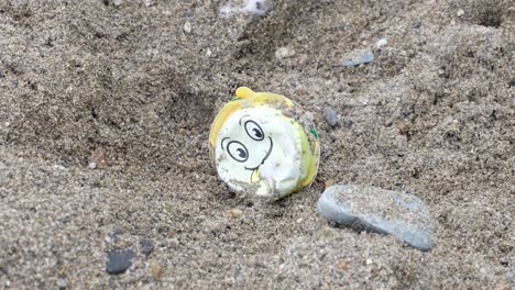 Cerca-De-Plástico-Oceánico-Con-Cara-Sonriente-Feliz-Tumbado-En-Una-Playa-De-Arena-Que-Contamina-El-Mar-Y-La-Costa-En-Un-Remoto-Destino-De-Isla-Tropical