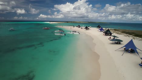 1Los-Roques-Archipel-Mit-Klarem-Türkisfarbenem-Wasser,-Weißem-Sandstrand,-Booten-Und-Besuchern-Unter-Zelten,-Luftaufnahme