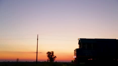 Silueta-De-Tren-Contra-Una-Vibrante-Puesta-De-Sol-En-El-Campo,-Temprano-En-La-Noche