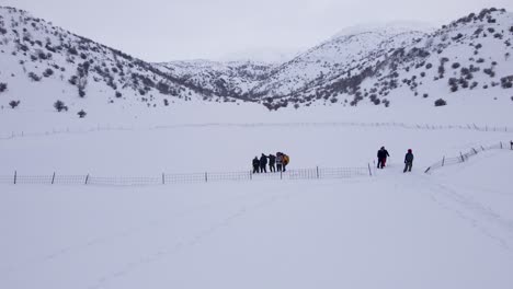 Drone-filming-men-waving-before-reverse-ascending-to-reveal-a-snow-covered-landscape