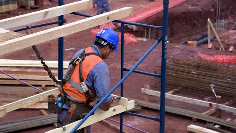 Bauarbeiter-In-Orangefarbener-Weste-Und-Blauem-Helm-Arbeiten-Tagsüber-Auf-Einem-Gerüst-Auf-Einer-Baustelle