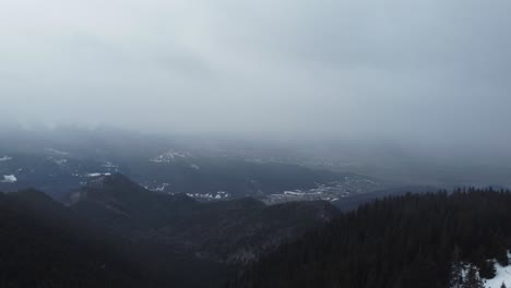 Increíble-Toma-Aérea-De-Montañas-Llenas-De-Pinos-Y-Nieve,-Y-Un-Cielo-Nublado-Durante-Una-Nevada-Invernal