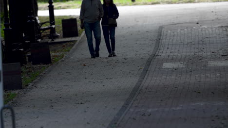 Ein-Paar-Geht-Auf-Einem-Kopfsteinpflasterweg-In-Einem-Park,-Aufgenommen-Von-Der-Hüfte-Abwärts,-Mit-Schwerpunkt-Auf-Bewegung-Und-Dem-Lässigen,-Alltäglichen-Charakter-Eines-Spaziergangs-In-Einer-Städtischen-Grünfläche