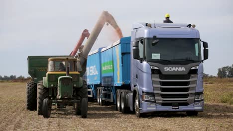 Grüne-Erntemaschine,-Die-Getreide-In-Einen-Blauen-LKW-Lädt,-Mit-Arbeiteraufsicht,-Tageslicht,-Landwirtschaftliche-Arbeitsszene,-Im-Freien