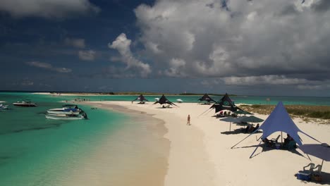 Archipiélago-De-Los-Roques-Con-Aguas-Cristalinas-De-Color-Turquesa,-Arenas-Blancas-Y-Visitantes-Bajo-Sombrillas,-Barcos-Anclados-Cerca,-Vista-Aérea