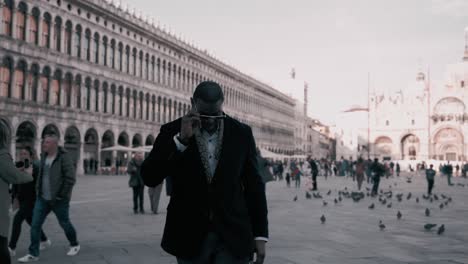 Hombre-Africano-Con-Un-Elegante-Traje-De-Lujo-Caminando-Fresco-Sobre-La-Famosa-Plaza-San-Marco-Junto-Al-Palacio-Ducal-En-Florencia-Italia-Como-Modelo-Rodeado-De-Turistas-Y-Pájaros