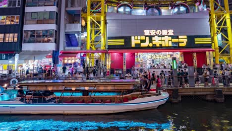 Nächtlicher-Zeitraffer-Von-Menschen,-Die-Vor-Dem-Riesenrad-Des-Ebisu-Turms-Auf-Ausflugsboote-Steigen,-Don-Quixote-Am-Dotonbori-Kanal,-Namba,-Osaka,-Japan