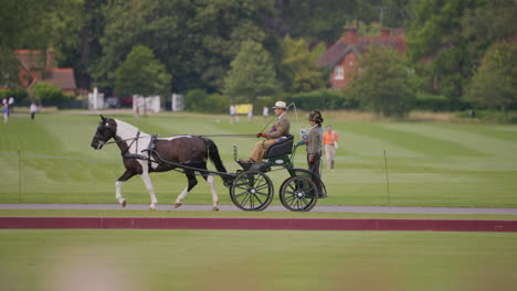 Man-drives-a-carriage-along-a-road-with-the-groom-hanging-on-the-back-the-horse-is-mixed-colour