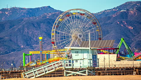 Fahrgeschäfte-Am-Santa-Monica-Pier,-Strand,-Rettungsschwimmerhütte-Und-Berge-Im-Hintergrund---Tageszeitraffer