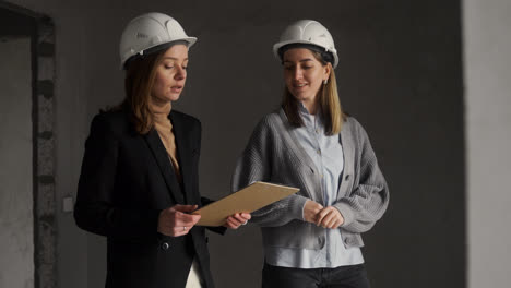 Frauen-Mit-Bauhelmen-Unterhalten-Sich-In-Einem-Leeren-Haus