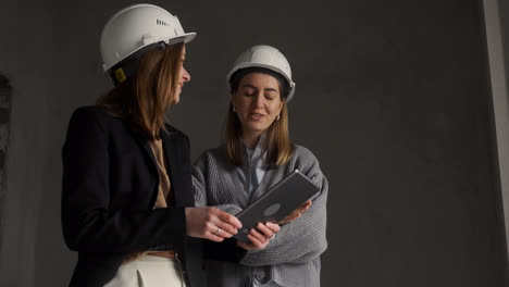 Mujeres-Con-Cascos-De-Seguridad-Hablando-En-Una-Casa-Vacía