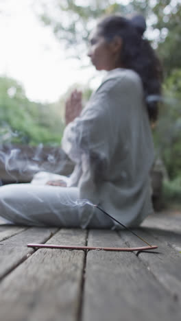 Video-Vertical-De-Una-Mujer-Birracial-Enfocada-Practicando-Yoga-En-Un-Jardín-Soleado,-Cámara-Lenta