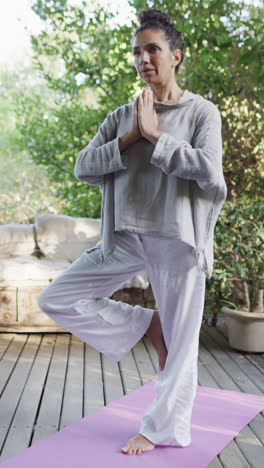 Vertical-video-of-focused-biracial-woman-practicing-yoga-on-sunny-terrace,-slow-motion