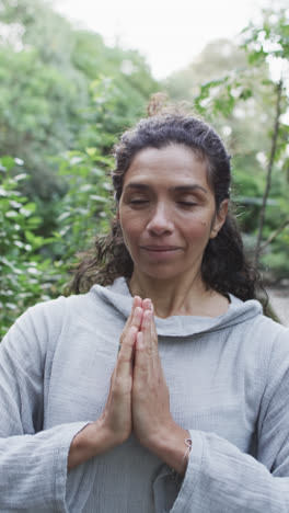 Vertical-video-of-focused-biracial-woman-practicing-yoga-in-sunny-garden,-slow-motion