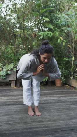 Video-Vertical-De-Una-Mujer-Birracial-Enfocada-Practicando-Yoga-En-Un-Jardín-Soleado,-Cámara-Lenta