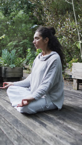 Vertical-video-of-focused-biracial-woman-practicing-yoga-in-sunny-garden,-slow-motion