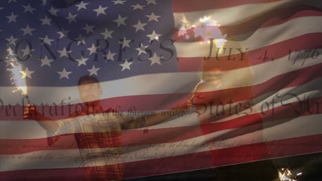 Caucasian-couple-using-fireworks-with-US-flag-waving-and-independence-declaration-foreground