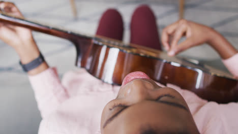 Overhead-view-of-african-american-woman-singing-and-playing-guitar-at-home