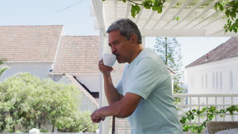 Senior-mixed-race-man-drinking-coffee-on-balcony-in-garden