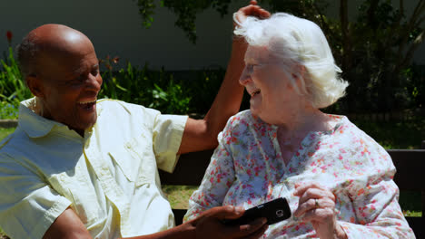 Vista-Frontal-De-Una-Pareja-Activa-De-Ancianos-De-Raza-Mixta-Usando-Un-Teléfono-Móvil-En-El-Jardín-De-Una-Residencia-De-Ancianos-4k