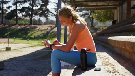 Vista-Lateral-De-Una-Atleta-Caucásica-Usando-Un-Reloj-Inteligente-En-Un-Recinto-Deportivo-4k