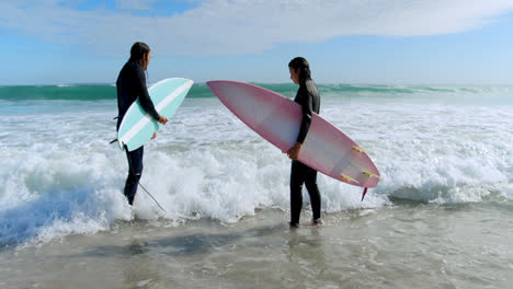 Pareja-De-Surfistas-Con-Tabla-De-Surf-Parada-En-El-Mar-4k