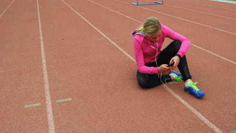 Front-view-of-Caucasian-female-athlete-listening-music-on-mobile-phone-at-sports-venue-4k