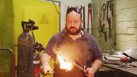 Caucasian-male-factory-worker-at-a-factory-standing-in-a-workshop,-holding-an-ignited-welding-gun