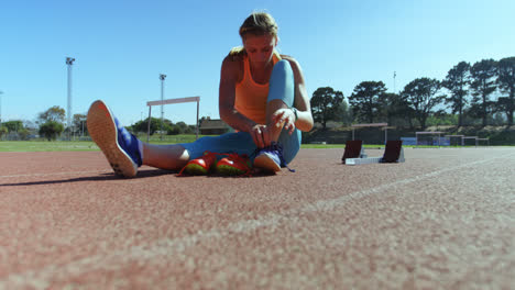 Vista-Frontal-De-Una-Atleta-Caucásica-Atando-Cordones-De-Zapatos-En-Un-Recinto-Deportivo-4k