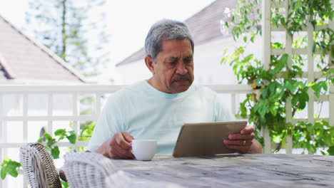 Älterer-Mann-Mit-Gemischter-Abstammung-Trinkt-Kaffee-Mit-Tablet-Im-Garten