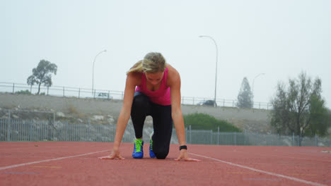 Vorderansicht-Einer-Kaukasischen-Sportlerin,-Die-Auf-Der-Laufstrecke-In-Einer-Sportstätte-Ihre-Startposition-Einnimmt,-4k