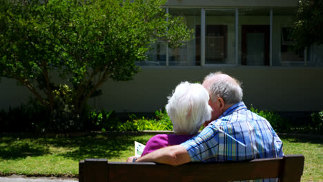 Vista-Trasera-De-Una-Pareja-De-Ancianos-Caucásicos-Activos-Mirando-Un-álbum-De-Fotos-En-El-Jardín-De-Una-Residencia-De-Ancianos-4k