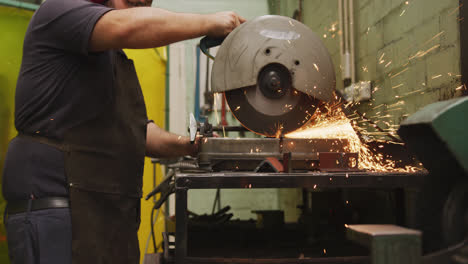 Caucasian-male-factory-worker-at-a-factory-standing-in-a-workshop,-standing-and-cutting-a-metal