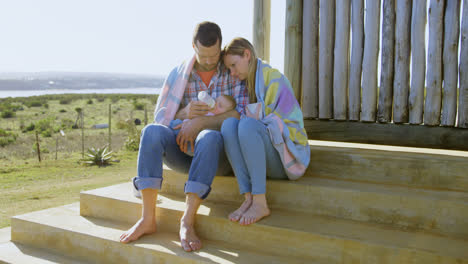 Front-view-of-mid-adult-caucasian-parents-feeding-their-baby-from-a-bottle-in-back-yard-of-home-4k