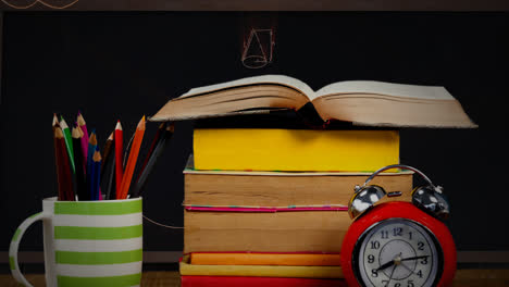 A-table-with-a-pile-of-books,-a-cup-with-pens,-and-an-alarm-clock-with-mathematical-equations-in-the