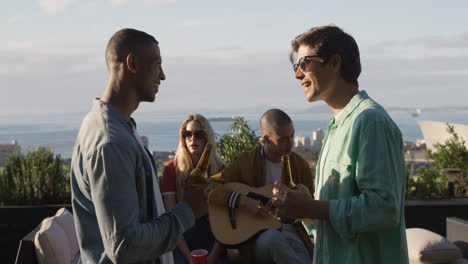 Un-Joven-Tocando-La-Guitarra-En-Una-Azotea-Con-Sus-Amigos.